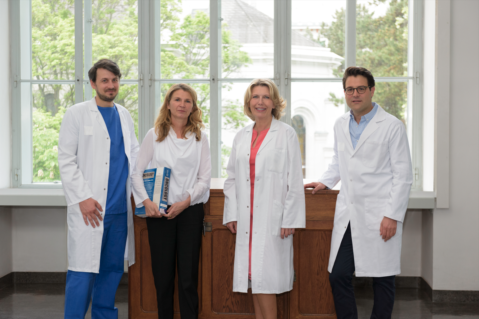 Leitungsteam der Cancer School: Johannes Gojo, Christine Németh, Gabriele Kornek und Stephan Polterauer stehen im Arztkittel vor einem Fenster im Jugendstilhörsaal ©CCC/Sabine Gruber