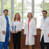 Leitungsteam der Cancer School: Johannes Gojo, Christine Németh, Gabriele Kornek und Stephan Polterauer stehen im Arztkittel vor einem Fenster im Jugendstilhörsaal ©CCC/Sabine Gruber